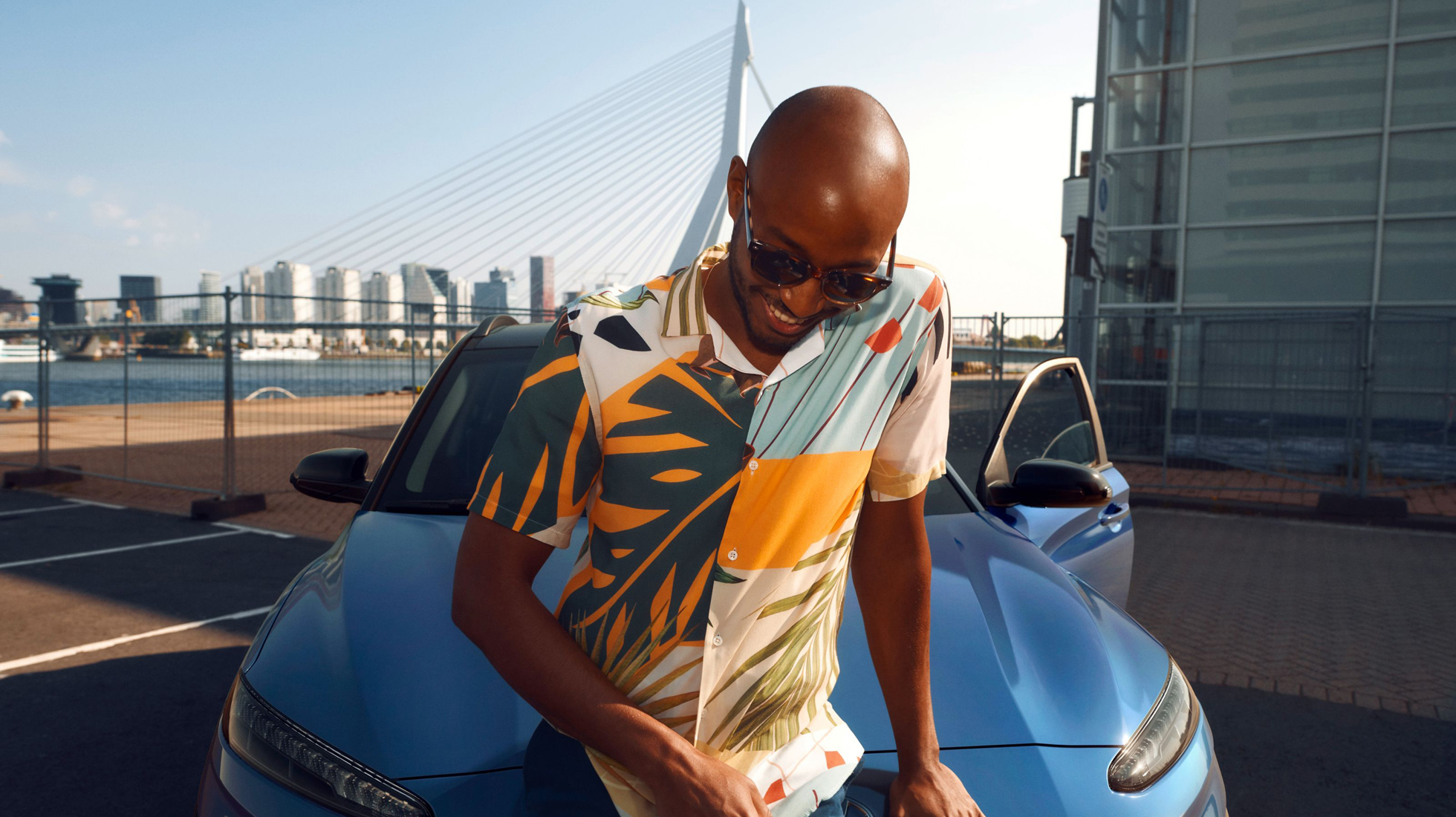 Muž sedící na kapotě nového modelu Hyundai KONA Hybrid v modrém odstínu Surfy Blue.